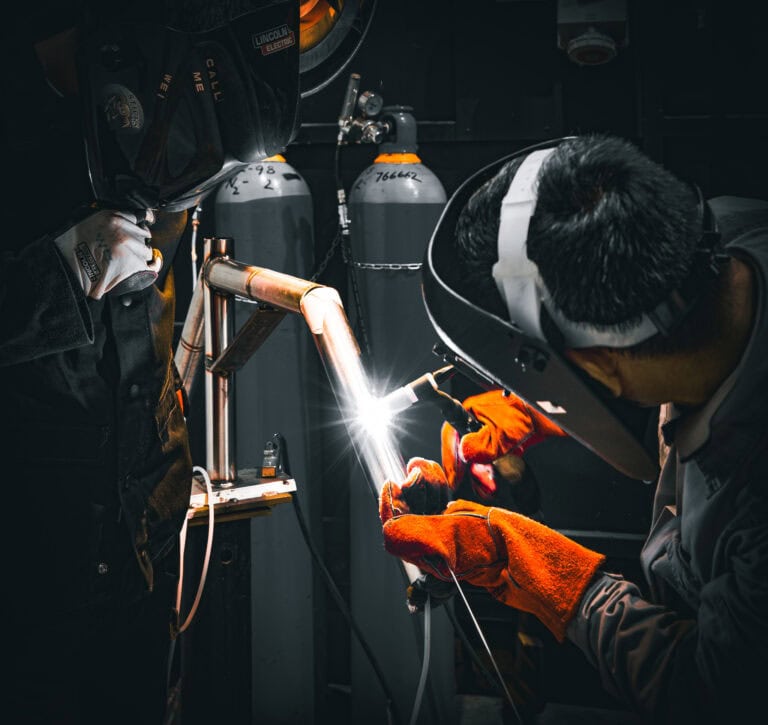 Engineers welding a stainless steel pipe joint. The ASTM A380 ferroxyl test is highly valued here.