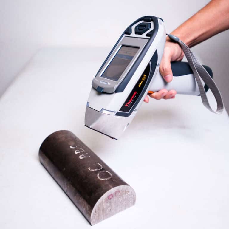 A handheld XRF analyser performing a PMI test on a metal sample to verify alloy composition.