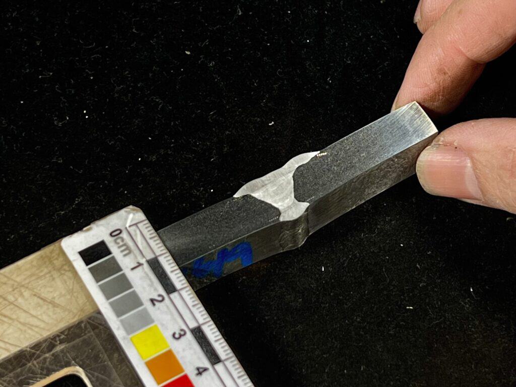 Macro etch weld test specimen with visible fusion line, held beside a measurement scale.